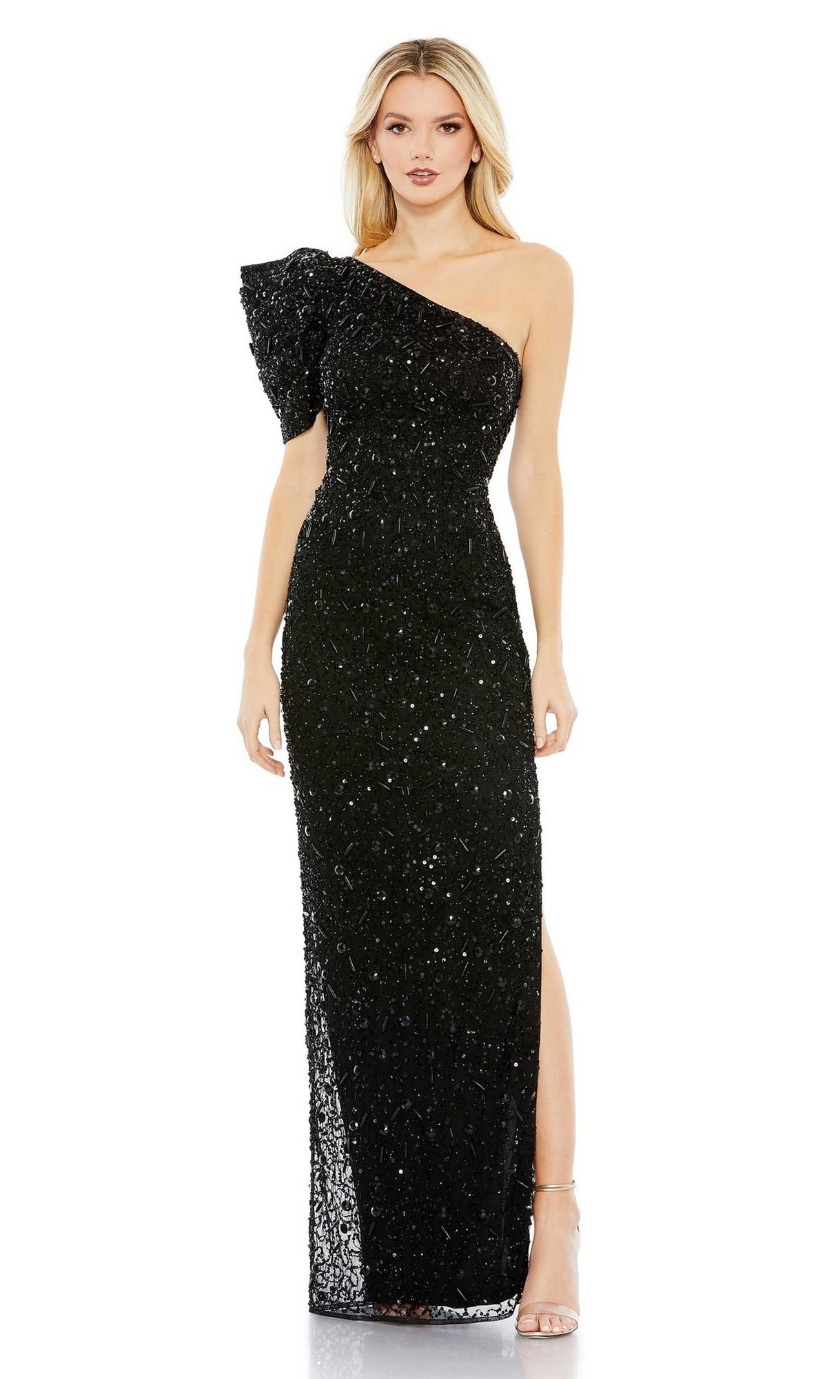 A woman stands in neutral heels against a white background, wearing the Long Formal Dress 10912 by Mac Duggal: a black, floor-length, one-shoulder gown with sequins and a side slit.